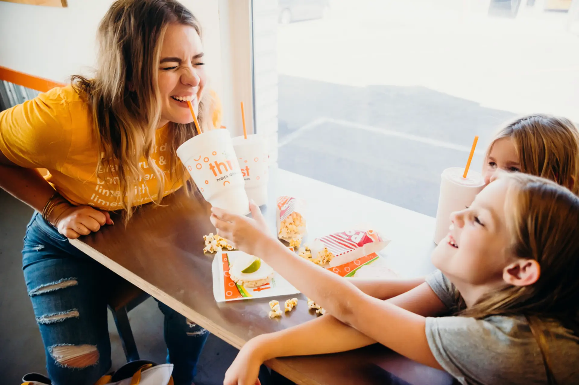 Mom and kids laughing over Thirst drinks and free popcorn at a Thirst table