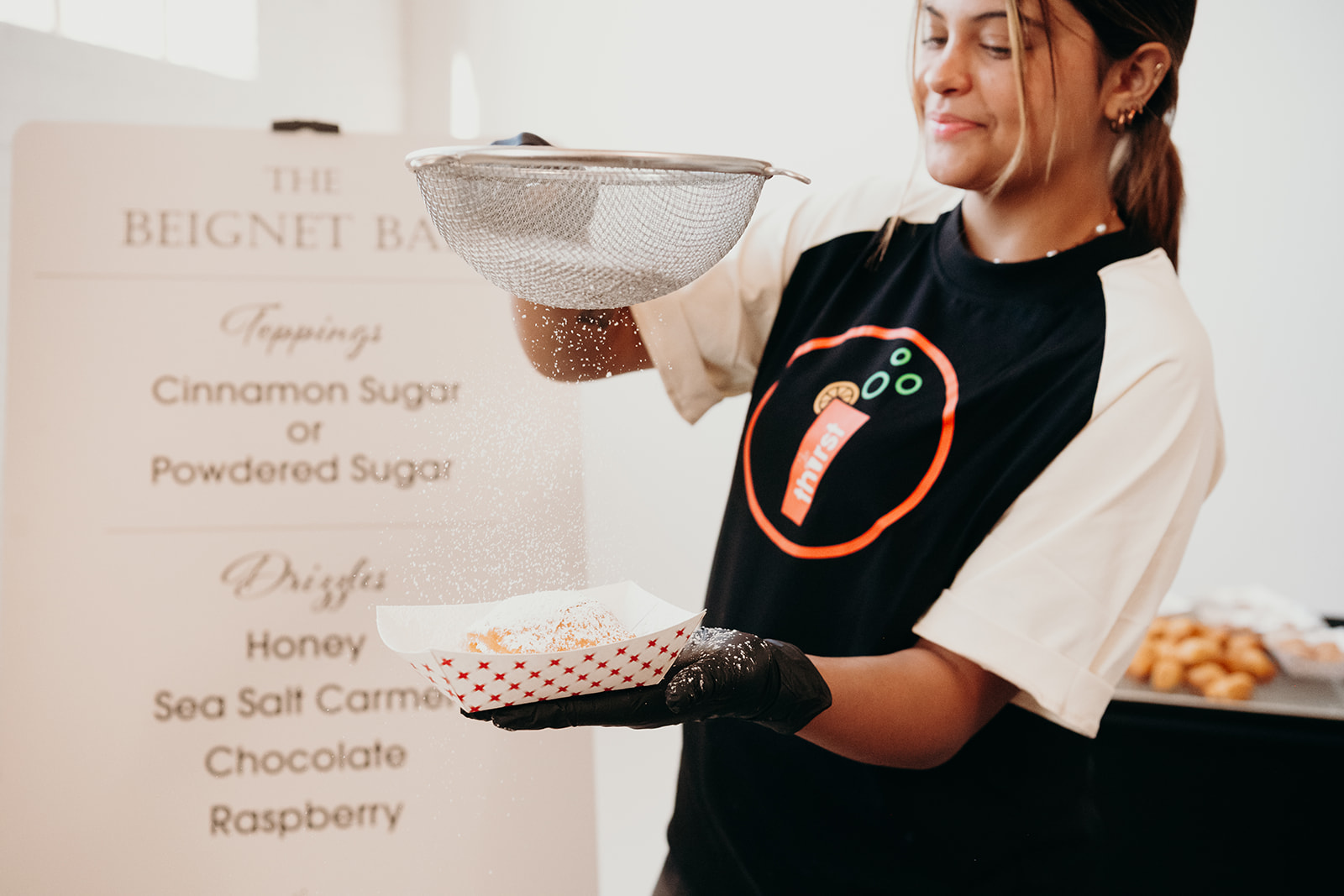 A Thirst team member dusting fresh-fried beignets with powdered sugar at the Beignet Bar