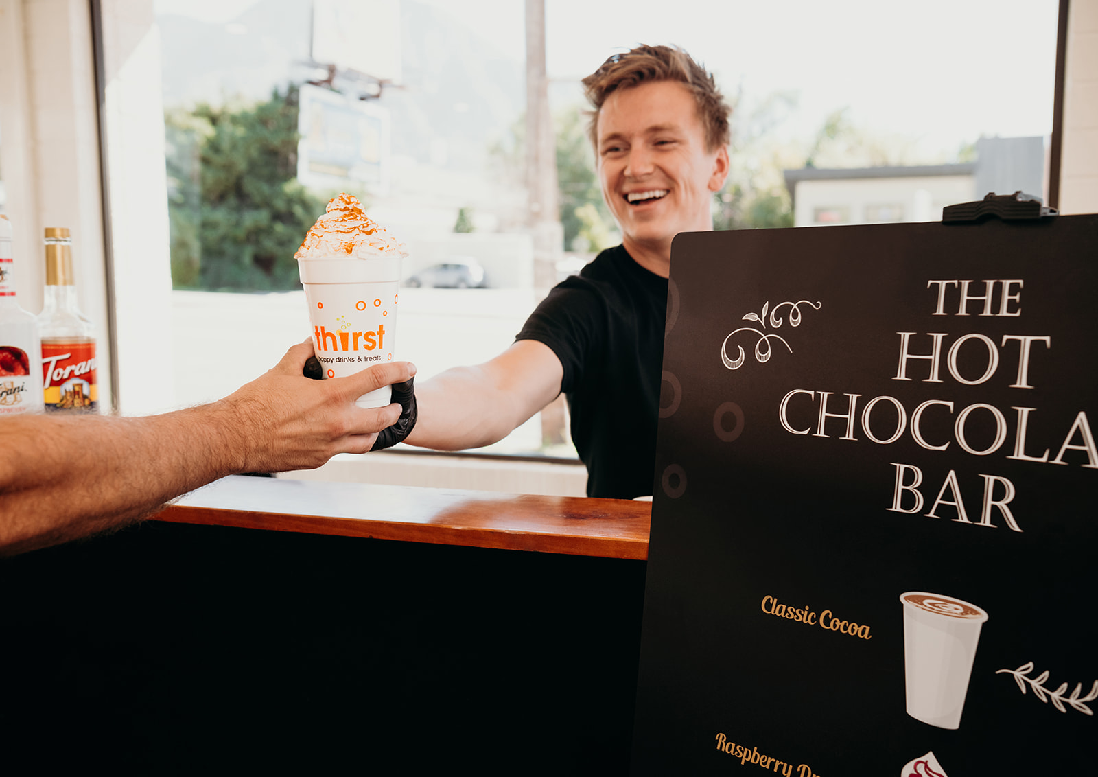 A Thirst team member handing a whipped cream hot chocolate across the Hot Chocolate Bar